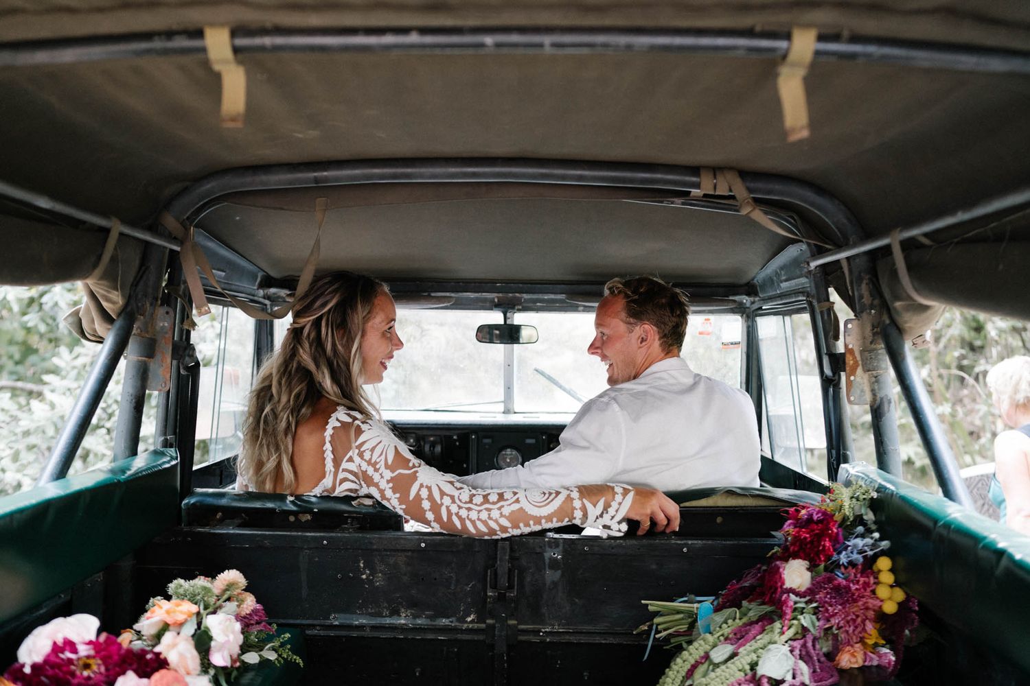 Two people sit together in a vintage vehicle decorated with colorful flowers in a romantic setting.
