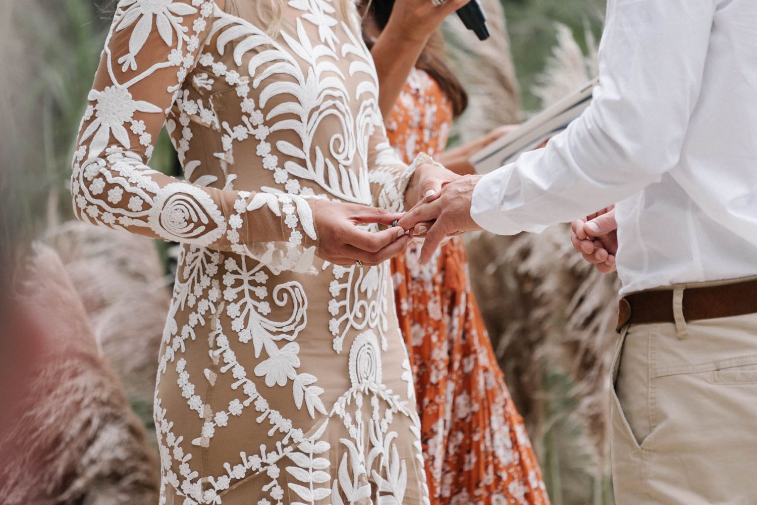 Close-up of elegant lace wedding dress with intricate floral patterns and detailed embroidery during outdoor ceremony.