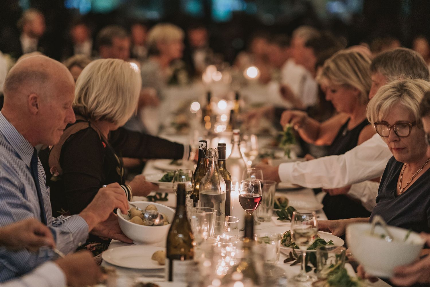 Guests enjoy an elegant dinner party with wine and candlelight at a long banquet table.