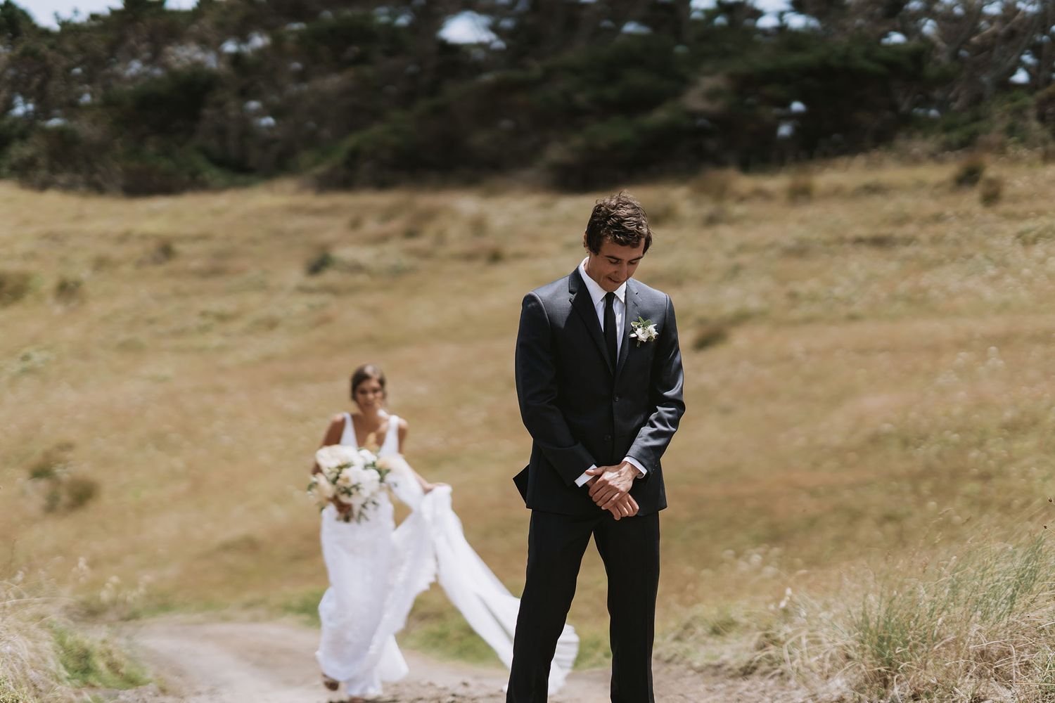 A couple walking together in formal attire through a scenic rural hillside on a sunny day.