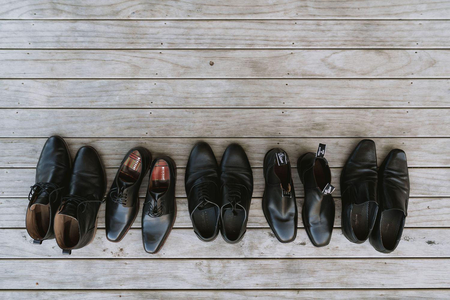 A row of black and brown dress shoes arranged neatly on a white wooden floor.