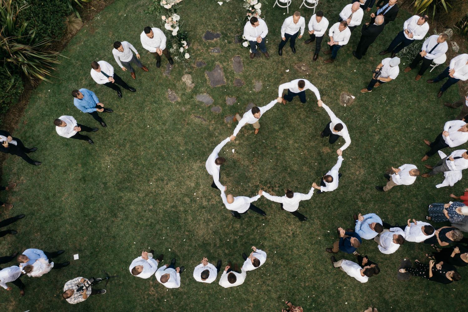 Aerial view of people wearing white clothing forming a circular formation on green grass.
