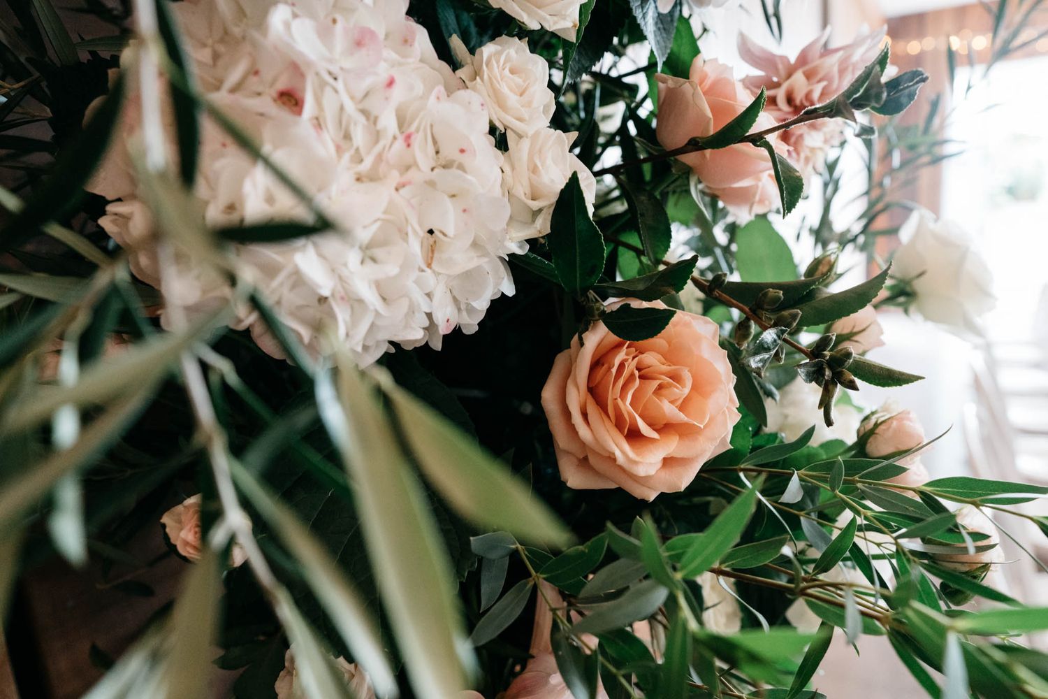 Close-up shot of a peachy rose and pale pink flowers with greenery in an elegant floral arrangement.