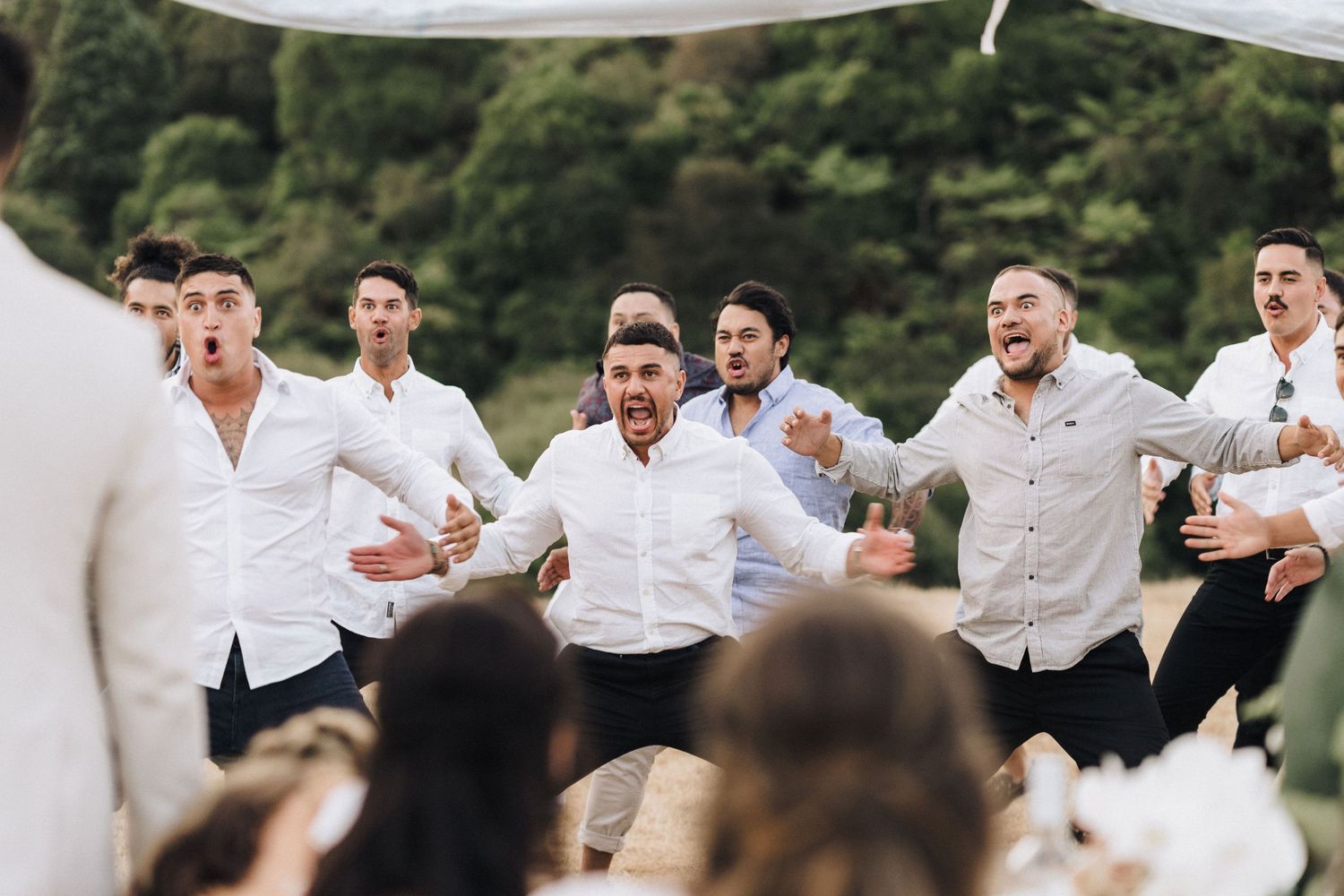 Group of men in white shirts perform energetic dance routine at outdoor wedding reception.