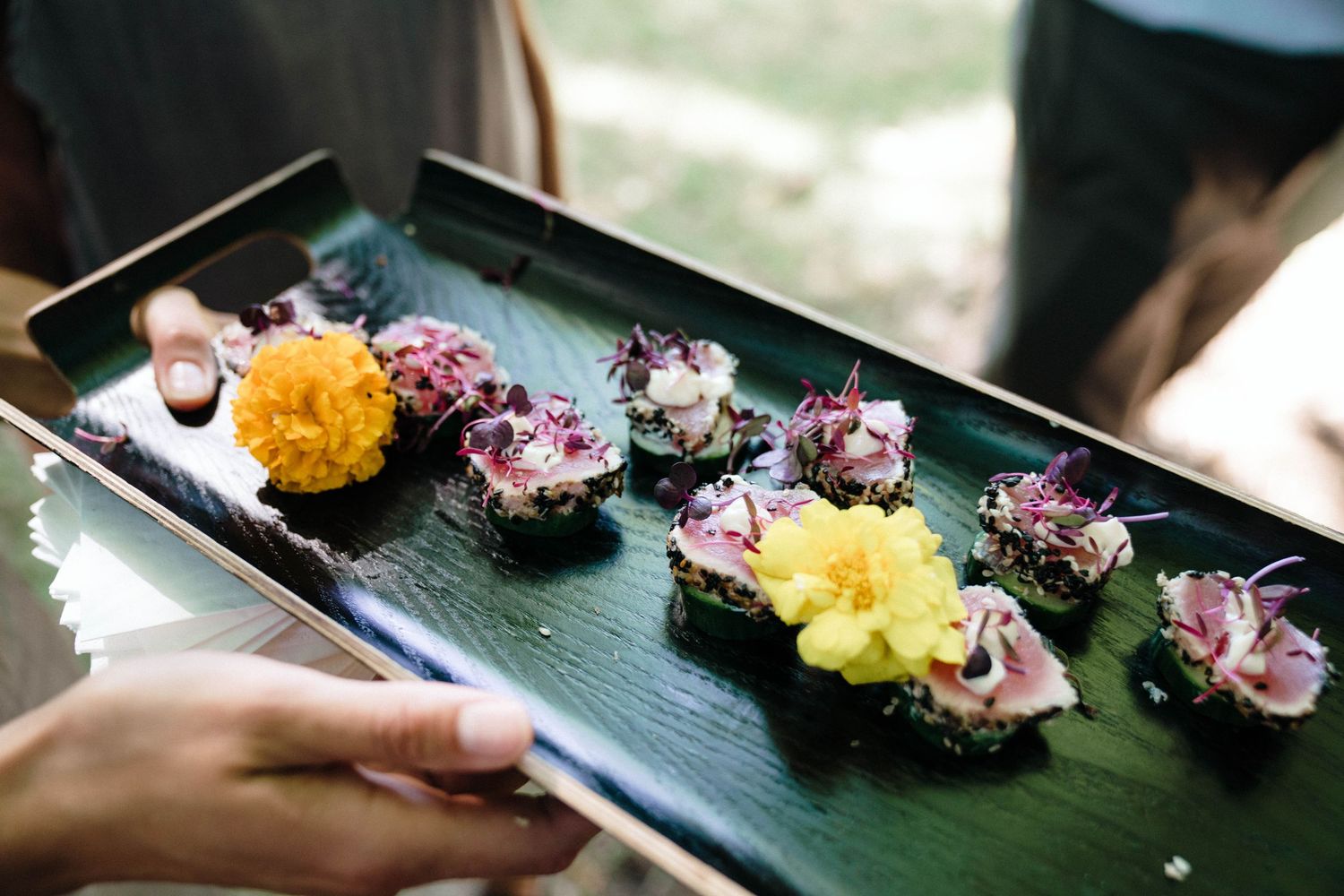 Elegant sushi appetizers arranged on banana leaves with yellow and purple garnishes served on a dark tray.
