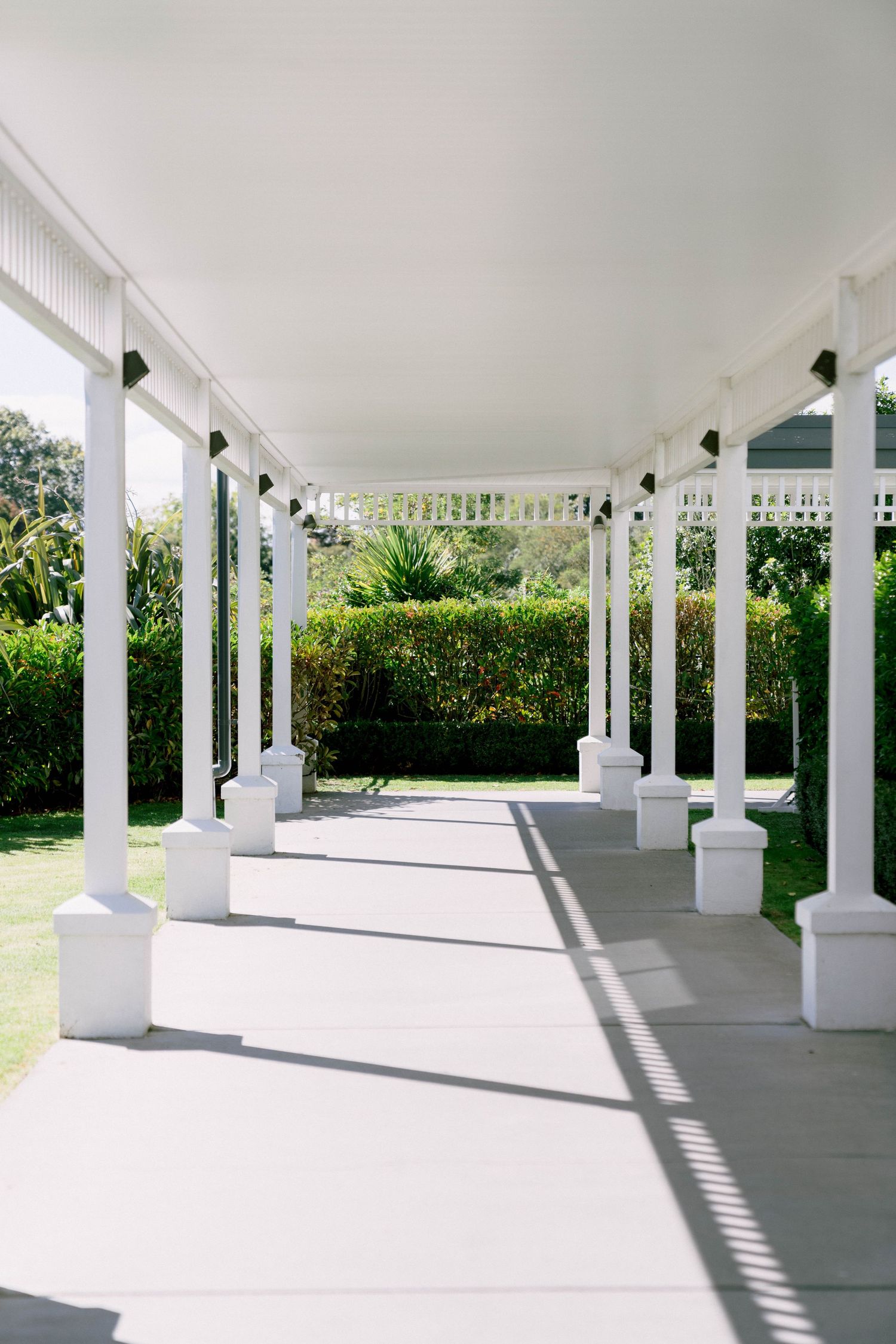 White pillared outdoor porch with clean concrete floor and green landscaping creates an elegant covered walkway.