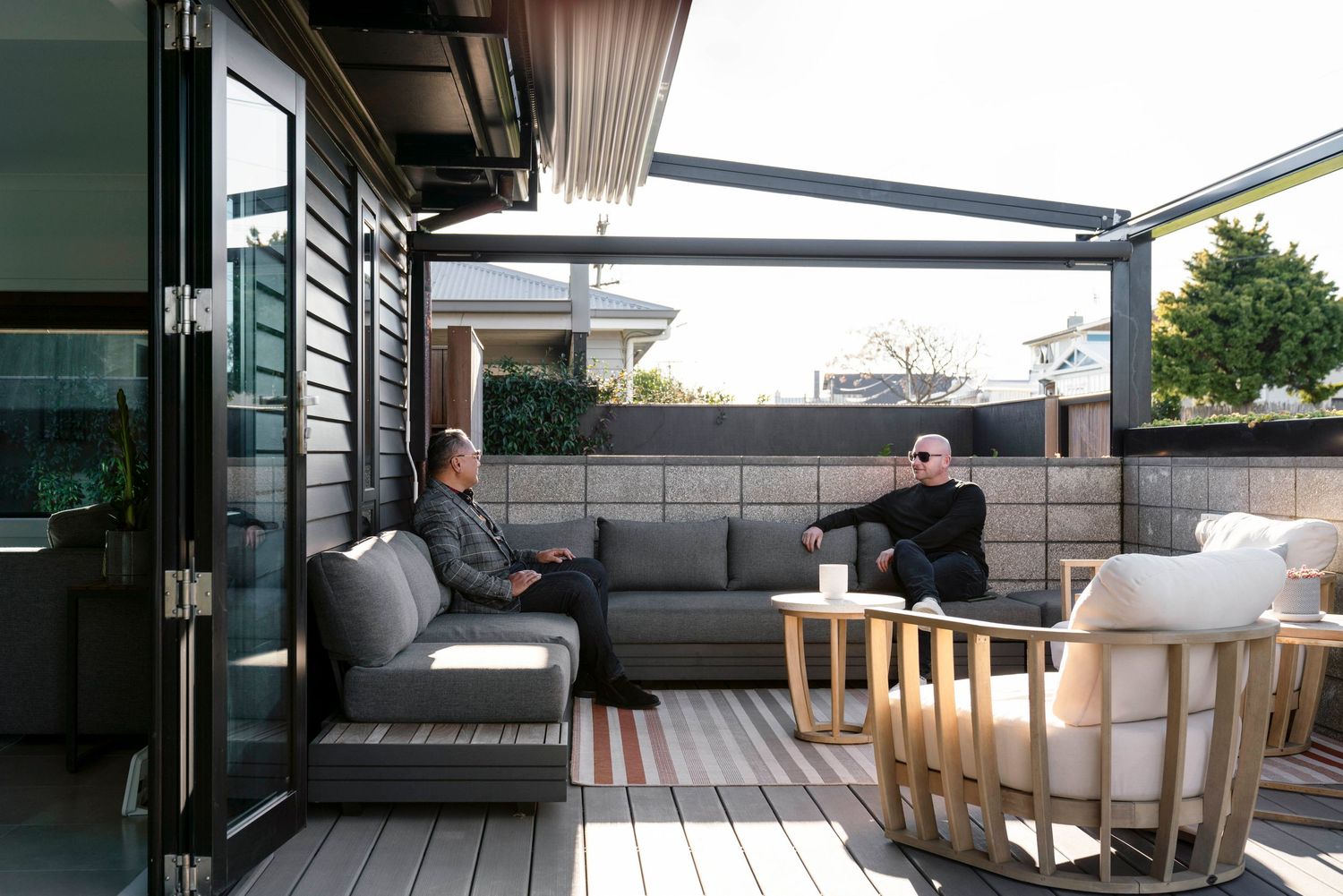 Two people relax on gray outdoor sectional furniture on a modern deck patio with wooden accents.