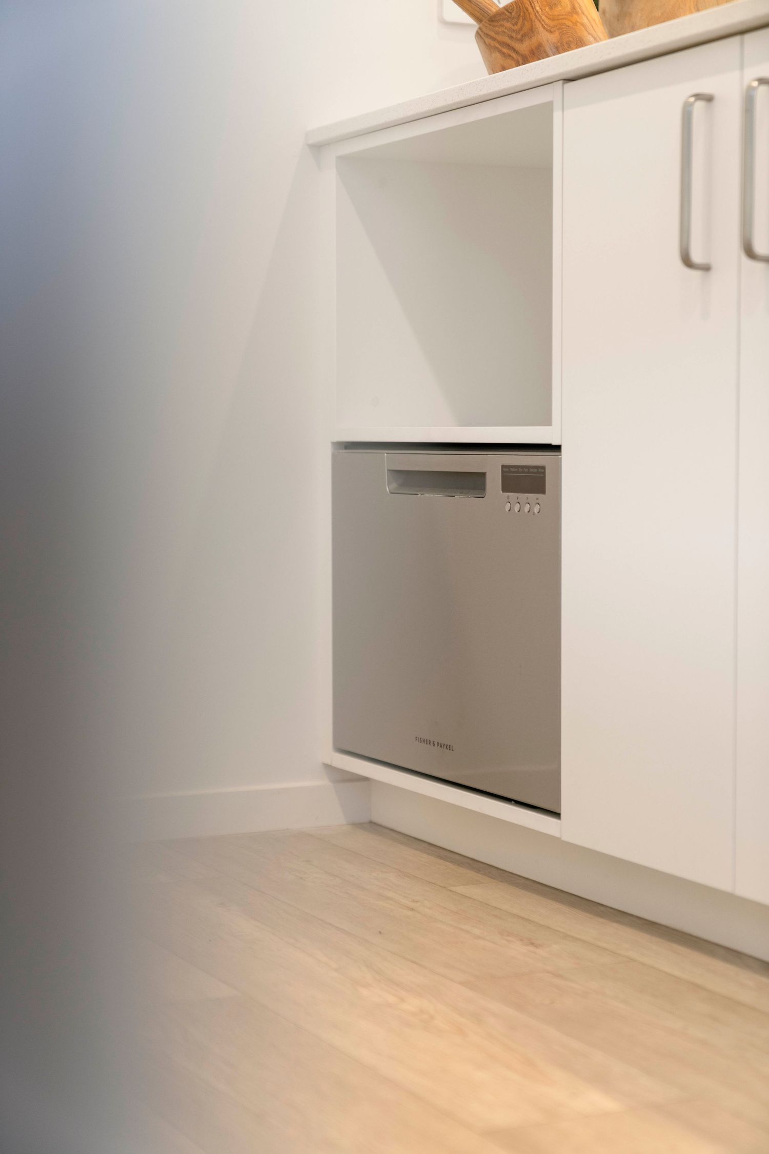 Clean white modern kitchen cabinets with light wood flooring and stainless steel appliances.