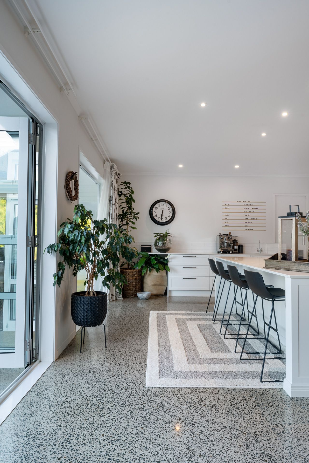 Modern kitchen with polished concrete floors, white cabinets, and bar seating featuring indoor plants and natural light.