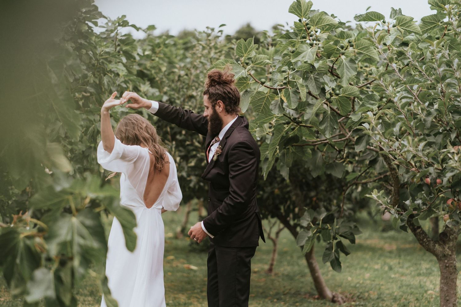 Couple shares a joyful moment while walking through an orchard on their wedding day.