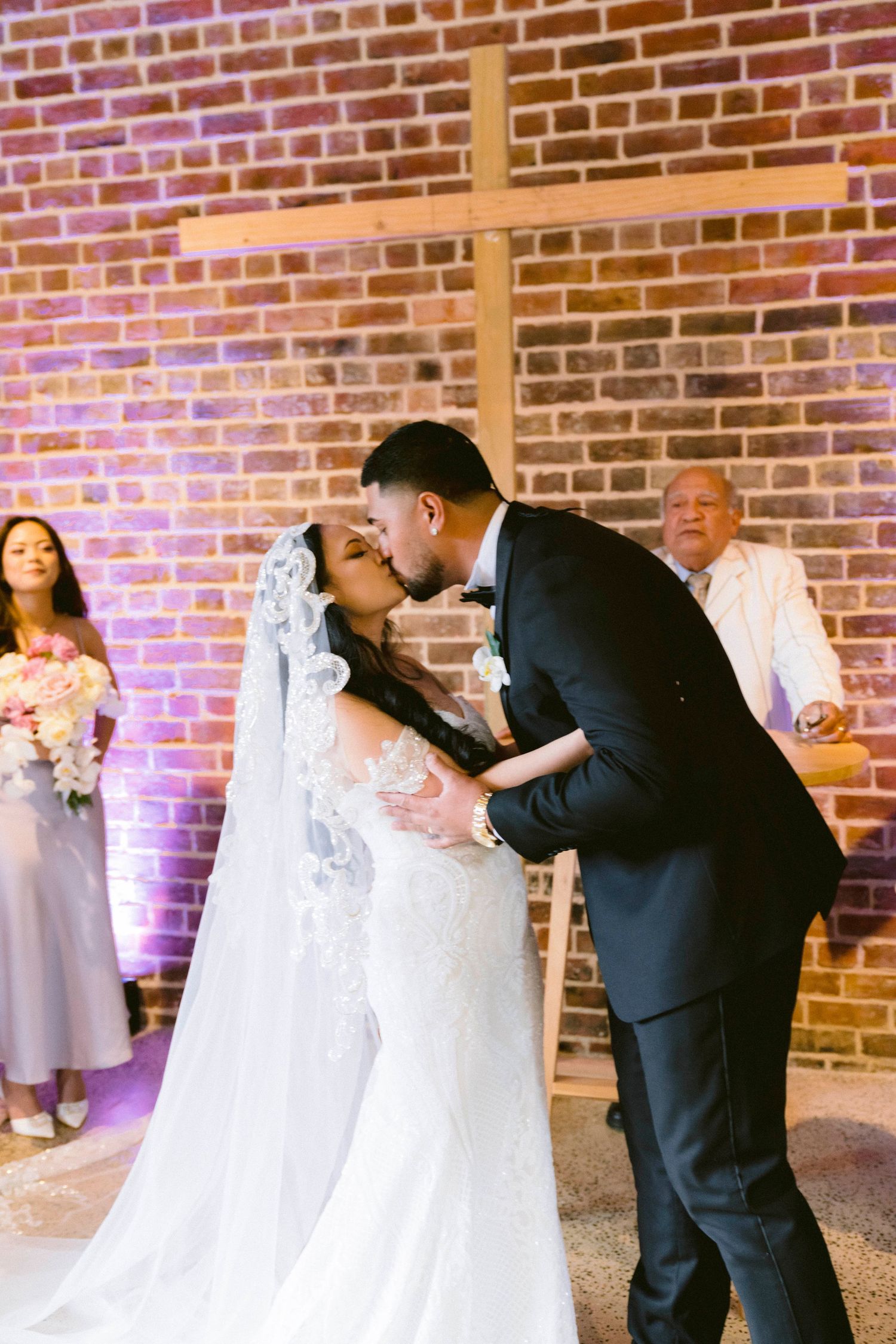 Newlyweds share romantic dance moves against exposed brick wall with purple uplighting at wedding reception.