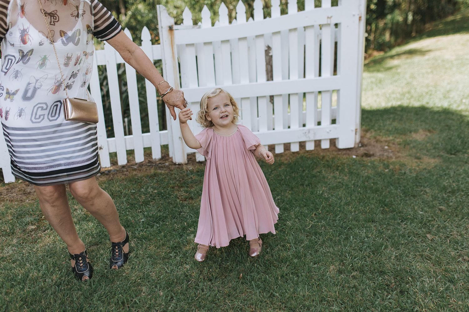 Four connected images show a young child in pink dress playing and twirling on grass near a white picket fence.