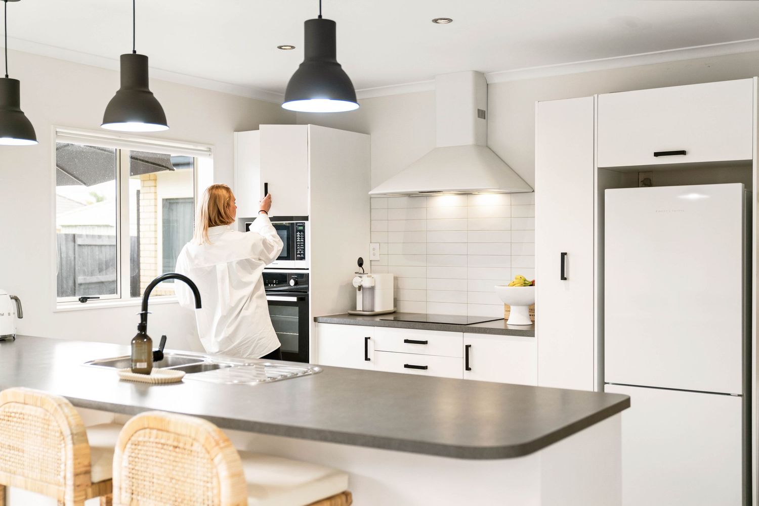 Bright contemporary kitchen interior with black pendant lights and wooden bar stools at counter.