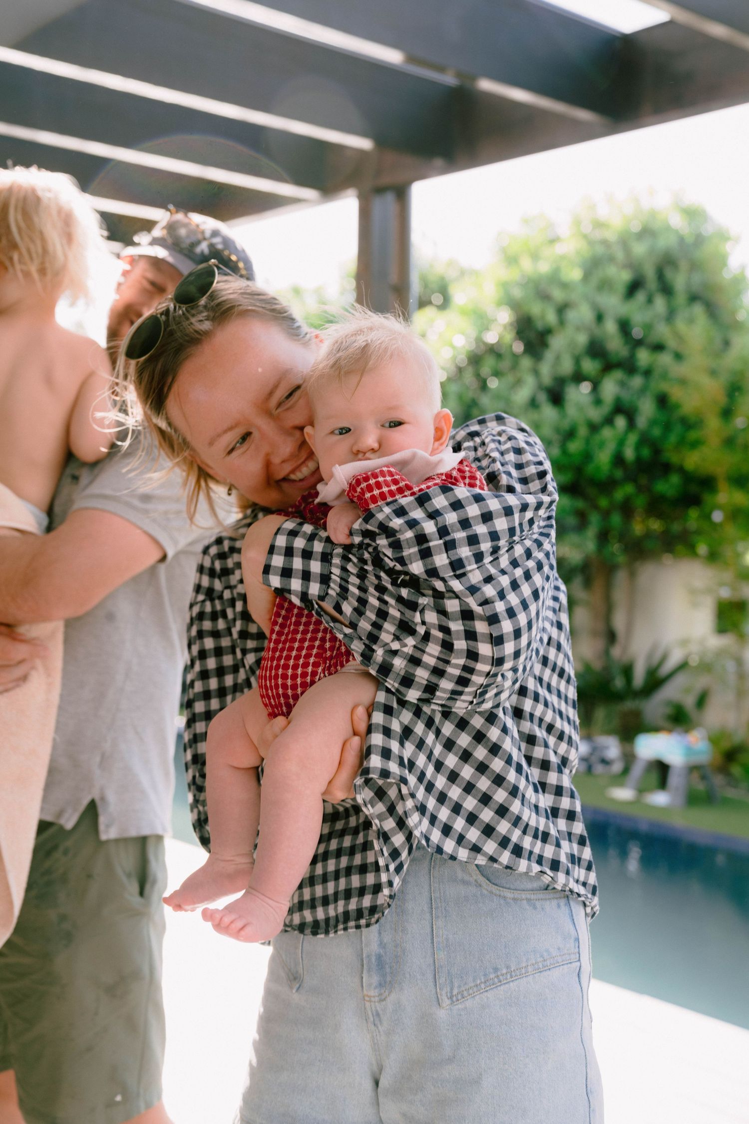 A young child in checkered clothing being held near a pool.