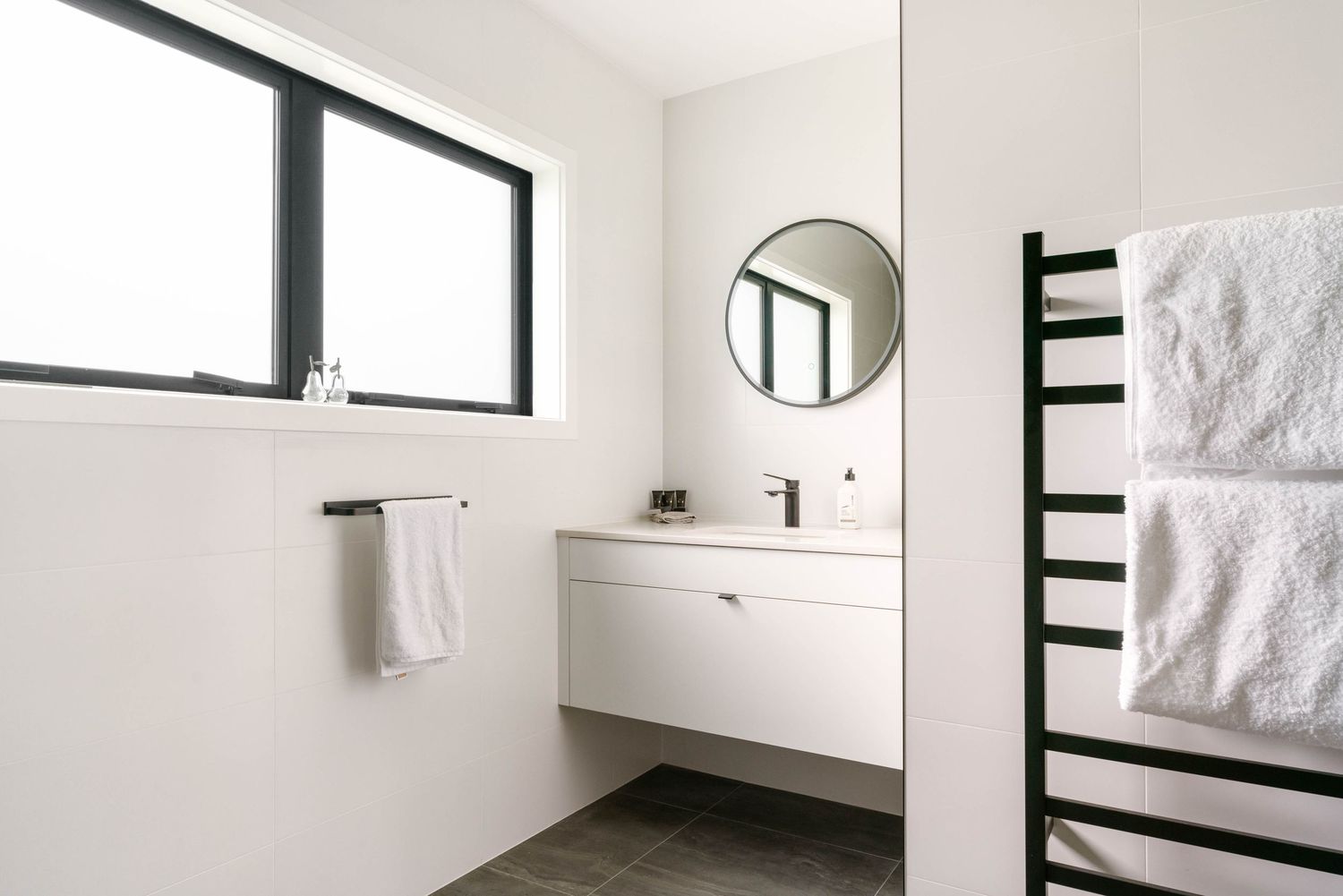 Contemporary white bathroom with sleek fixtures, floating vanity, and natural light from high windows.