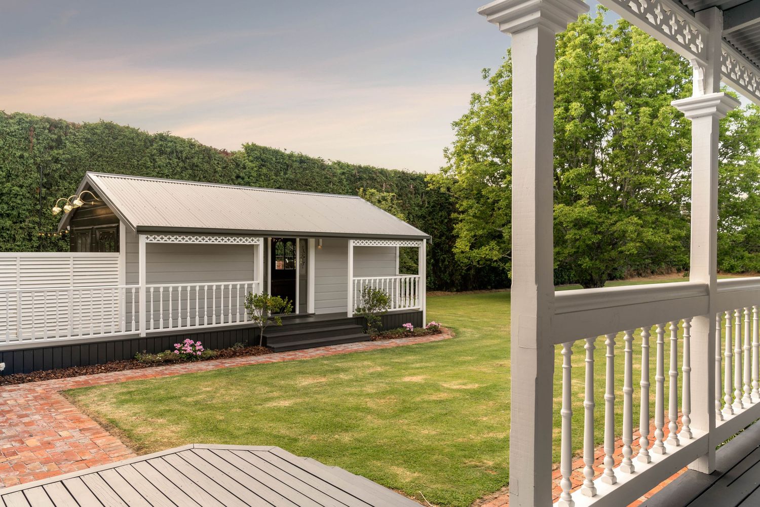 Spacious wraparound porch with white railings and columns overlooking a manicured lawn.