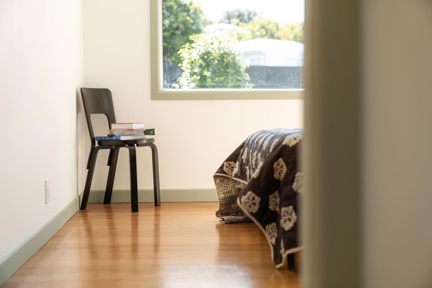 Empty room with hardwood flooring, single black chair against wall, and window letting in natural light.