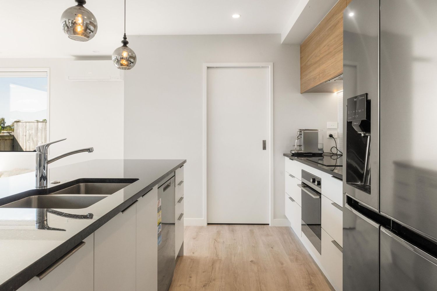 Modern white kitchen with light wood floors featuring a sleek black countertop and chrome pendant lighting.