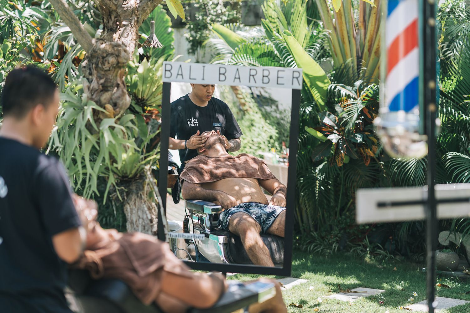 Tropical garden setting with barber shop sign and outdoor seating area.