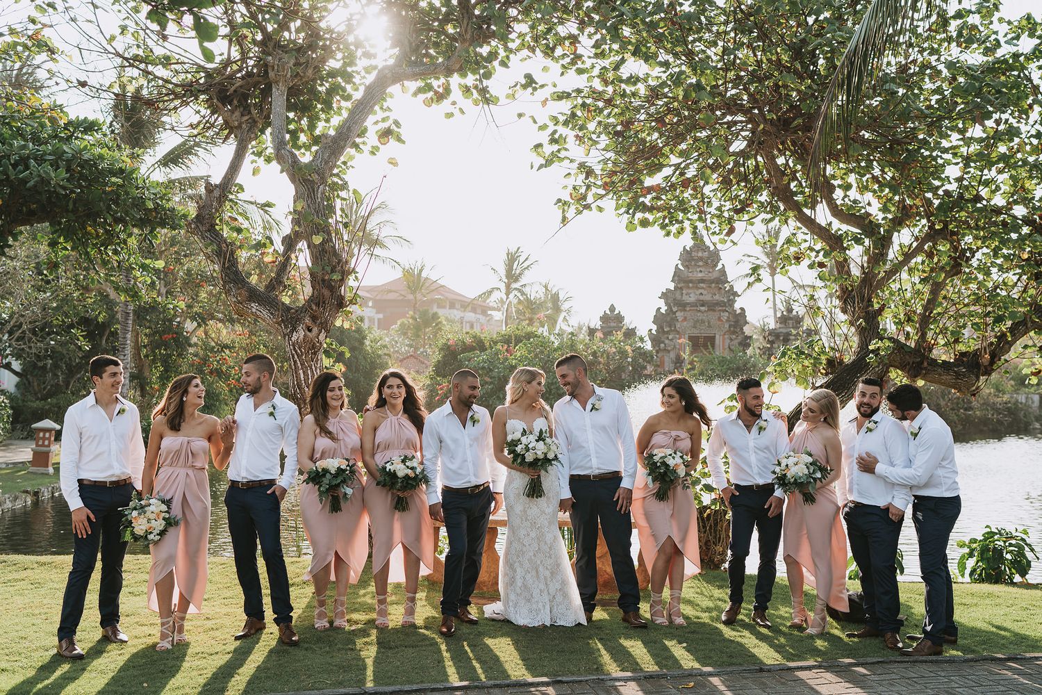 Wedding party poses for a group photo in front of a scenic lake and trees.