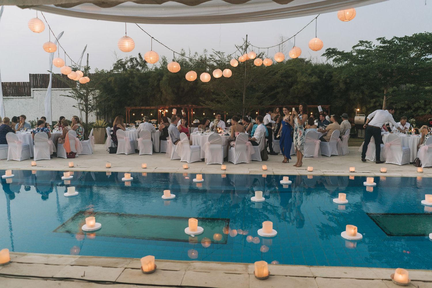 Outdoor evening wedding reception with paper lanterns glowing over a pool.