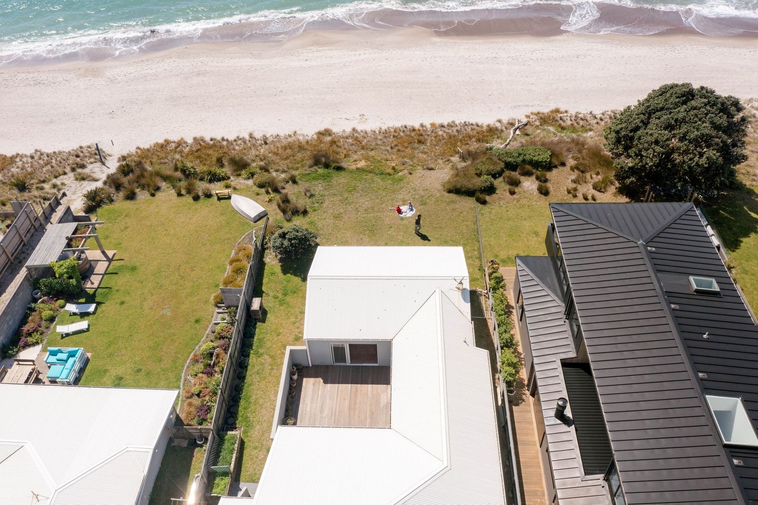 Aerial view of modern coastal homes with dark gray roofs and white walls aligned along a beachfront property.