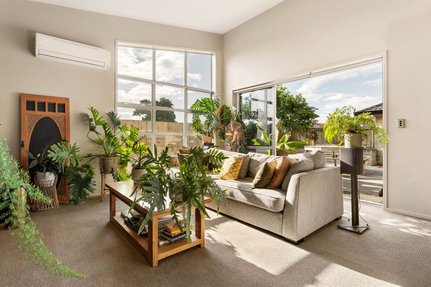 Modern living room featuring houseplants on wooden shelves, a gray sofa, and large windows letting in natural light.
