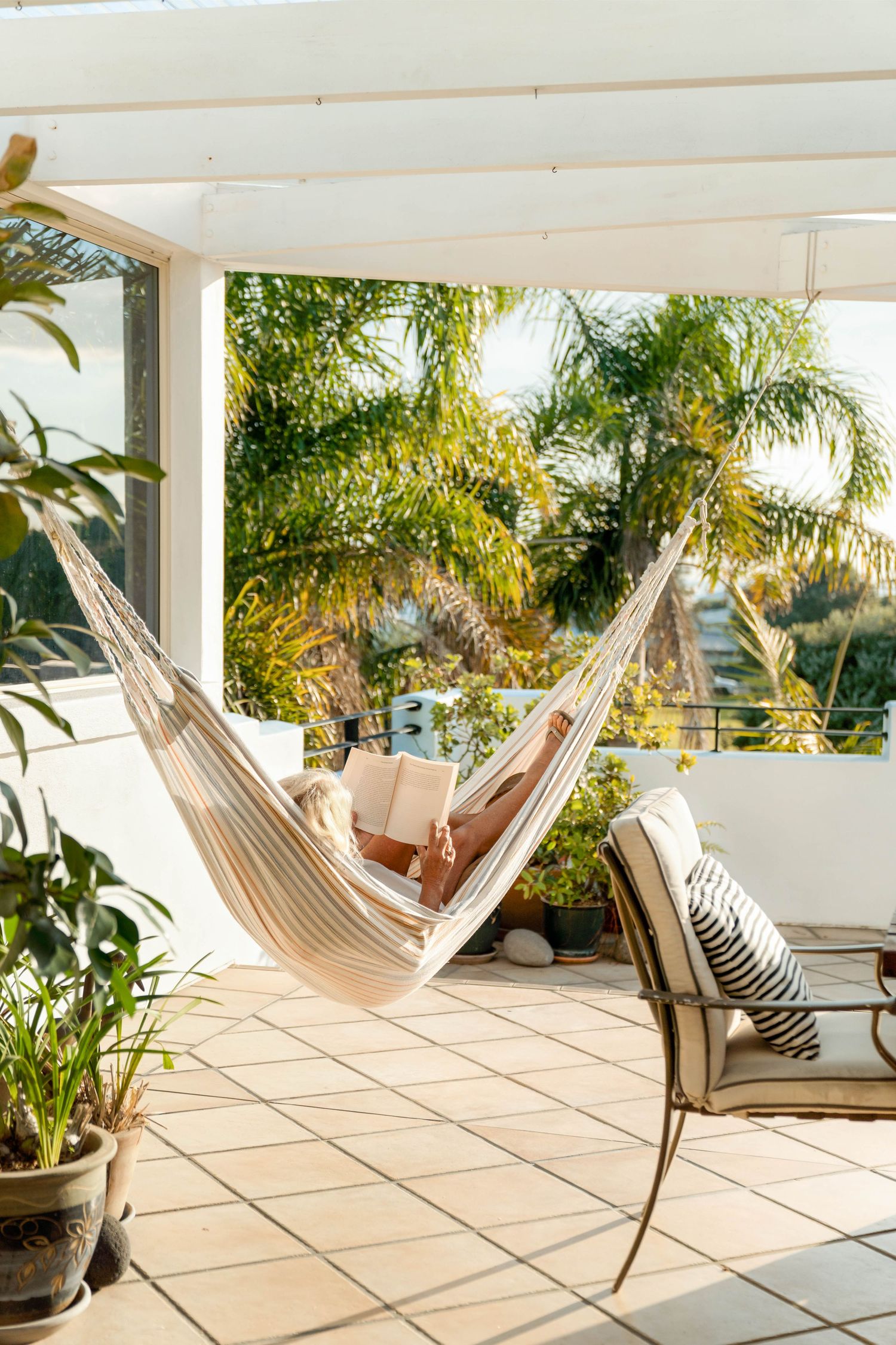 Cozy striped hammock on a sunny patio with palm trees and white columns creating a relaxing outdoor space.