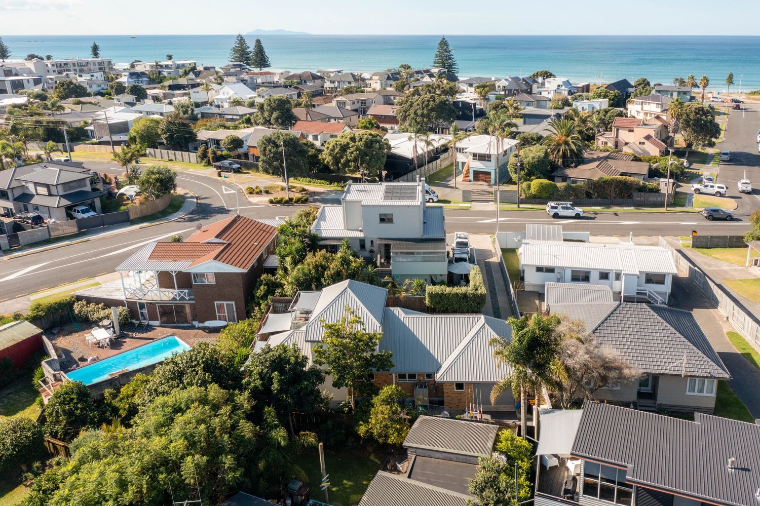Aerial view of beachside suburban homes with swimming pools near Mount Maunganui coastline in New Zealand.