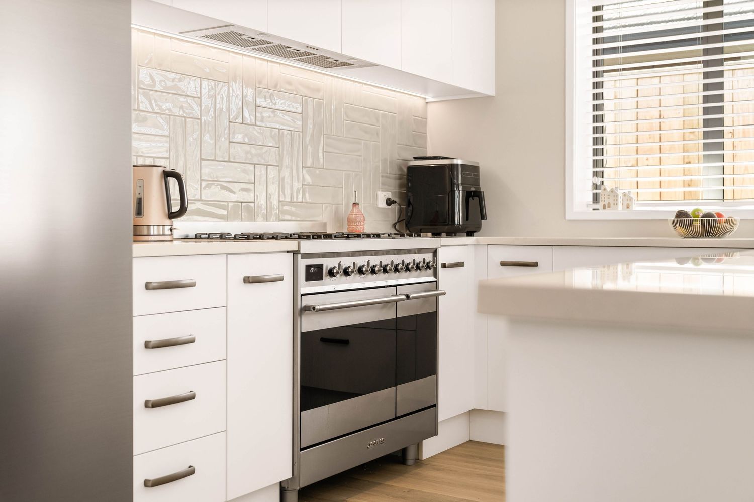 Clean white kitchen featuring modern appliances and horizontal window blinds.