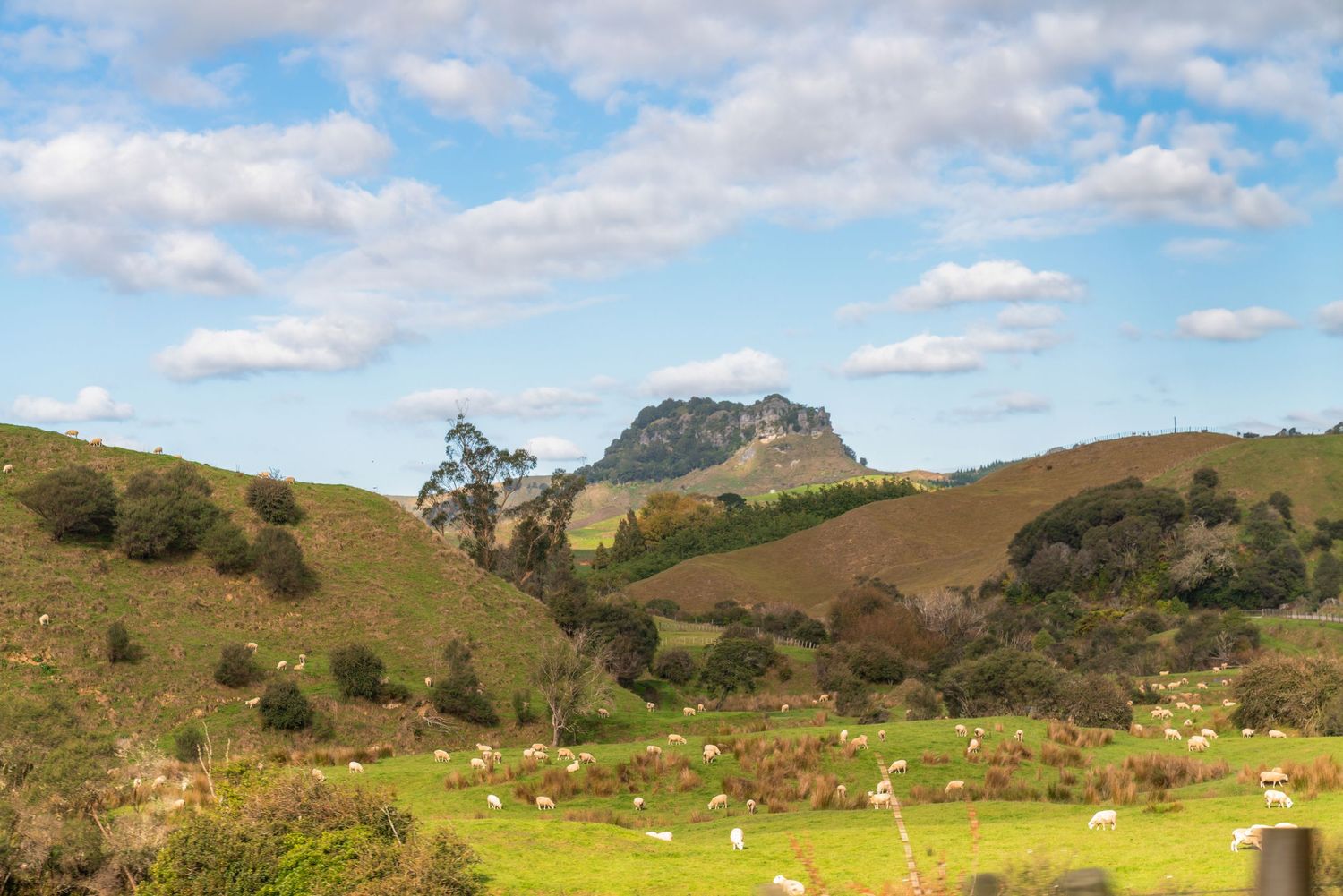 Scenic landscape of green rolling hills and mountains under partly cloudy blue skies.