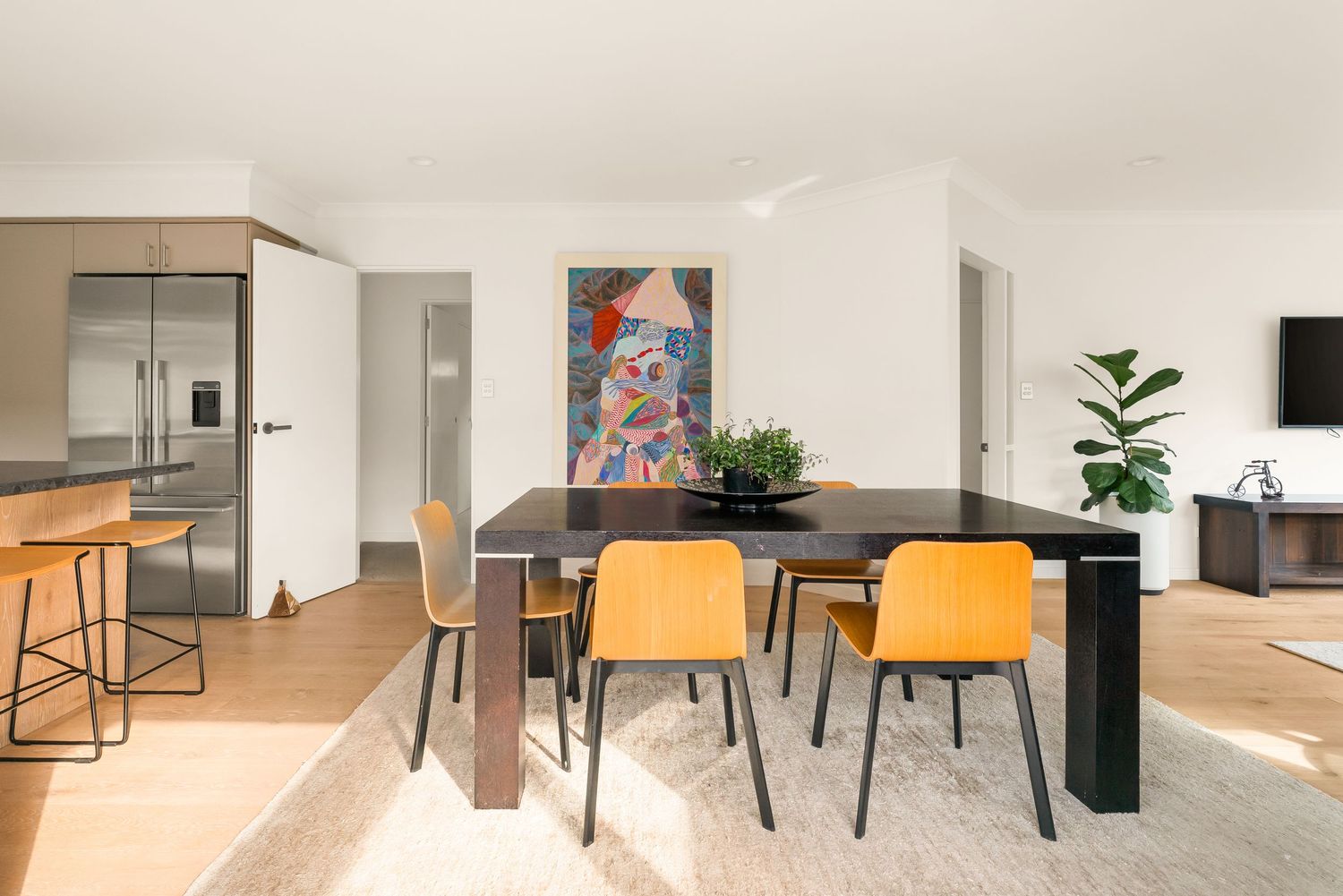 Open concept dining space with black table, orange chairs and colorful abstract wall art.