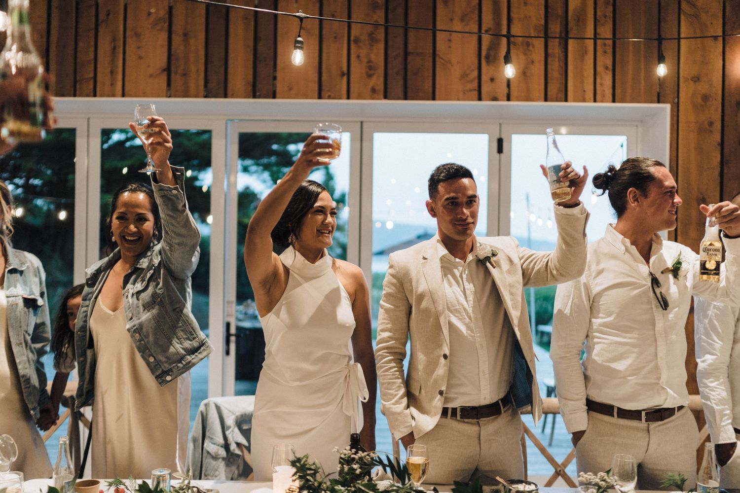 Wedding party members raise their glasses in celebration at a rustic barn reception venue.