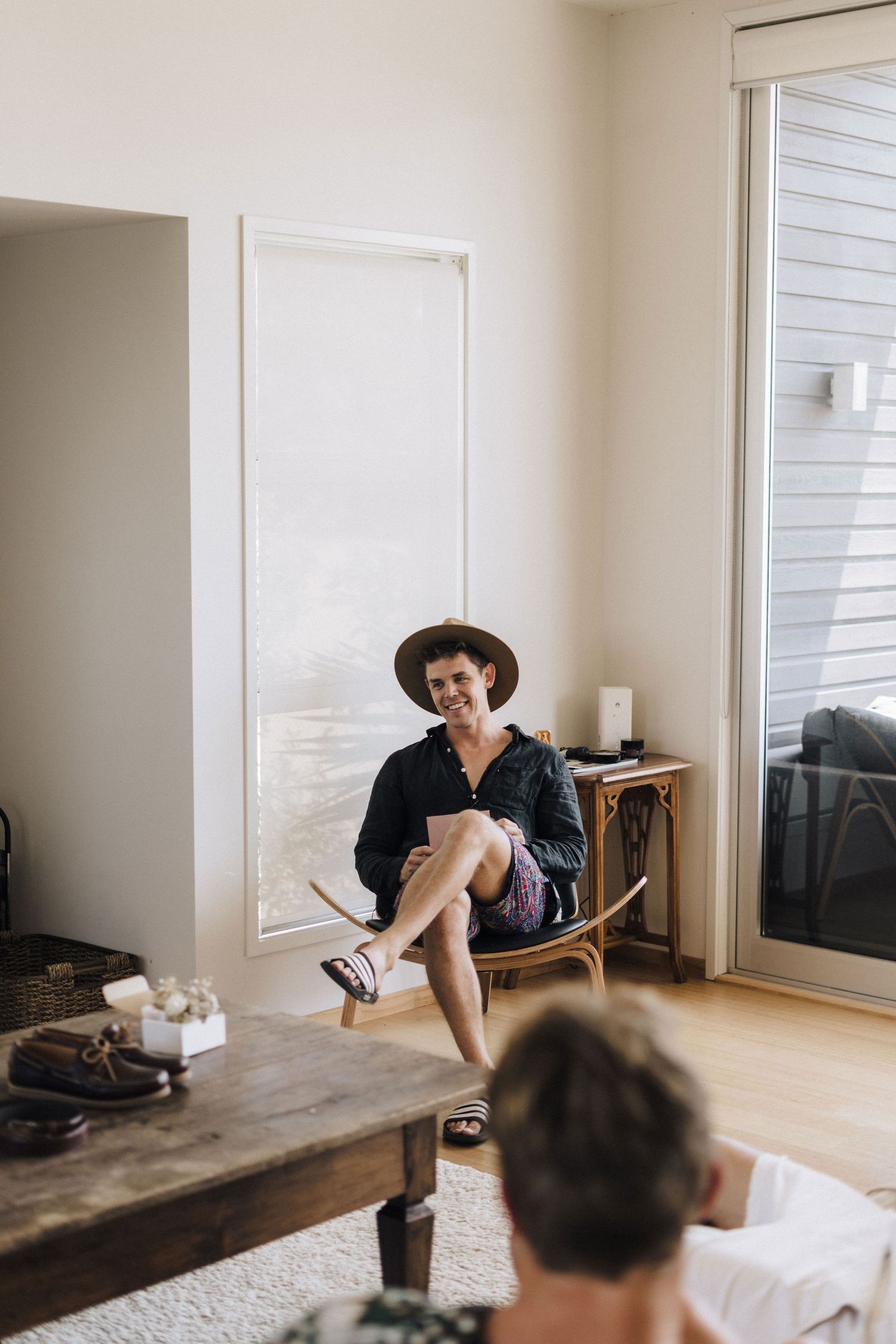 Person in black outfit and hat relaxing in a modern living room with natural light streaming through windows.