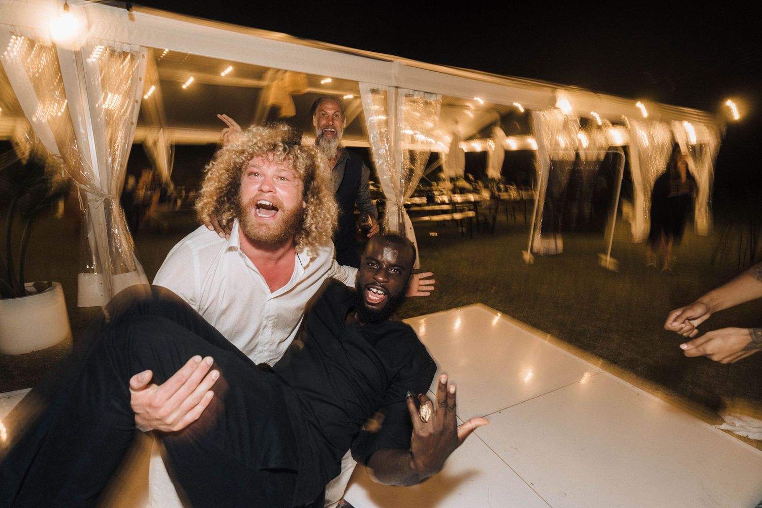 Lively dance floor moment at nighttime wedding reception under tent.