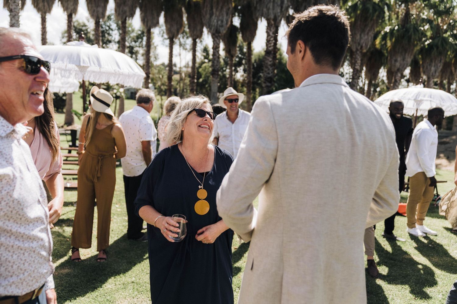 Wedding guests mingle and chat during outdoor reception under palm trees.