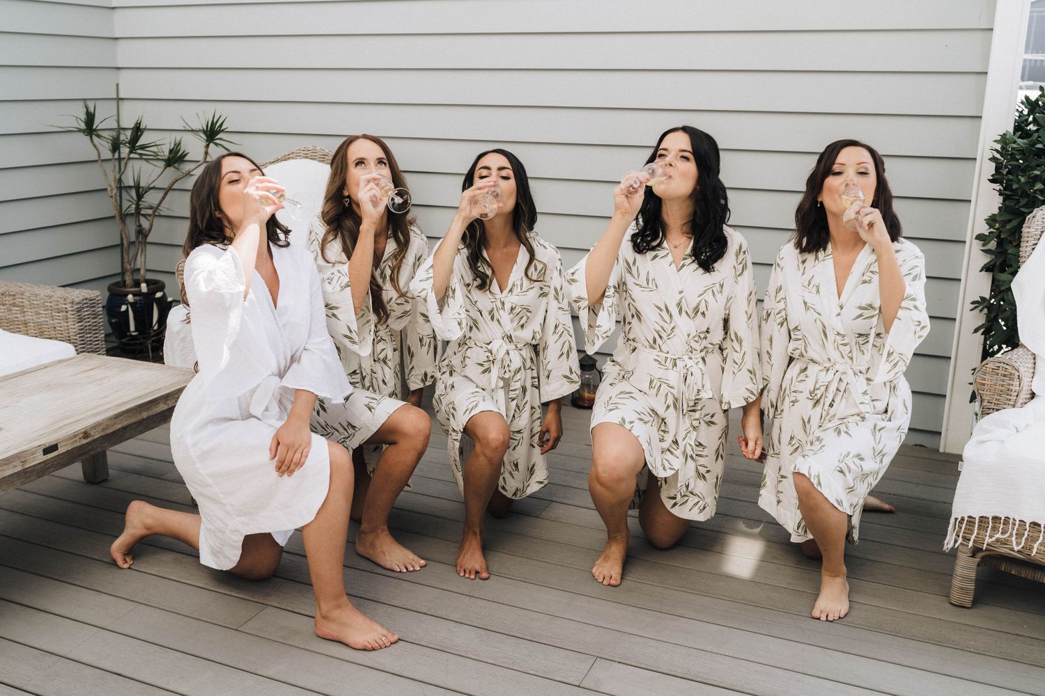 Group sitting together on white porch wearing matching light colored dresses.