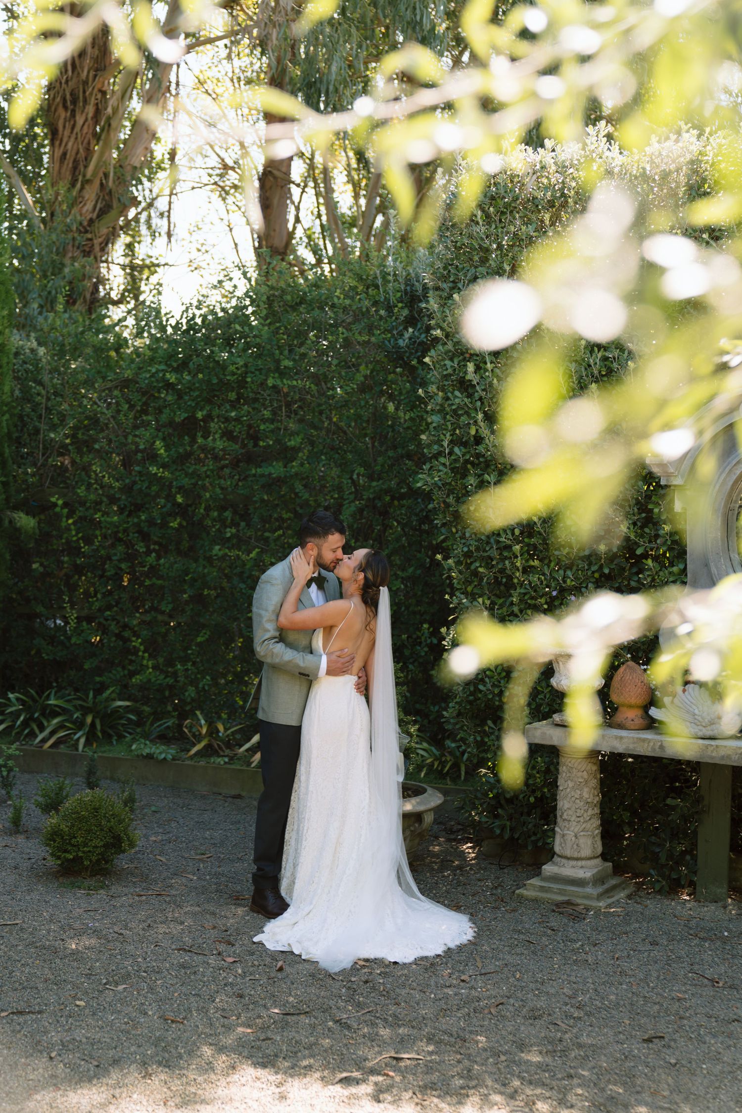 Bride and groom share a romantic kiss in a lush garden setting, bride wearing elegant white gown with veil.