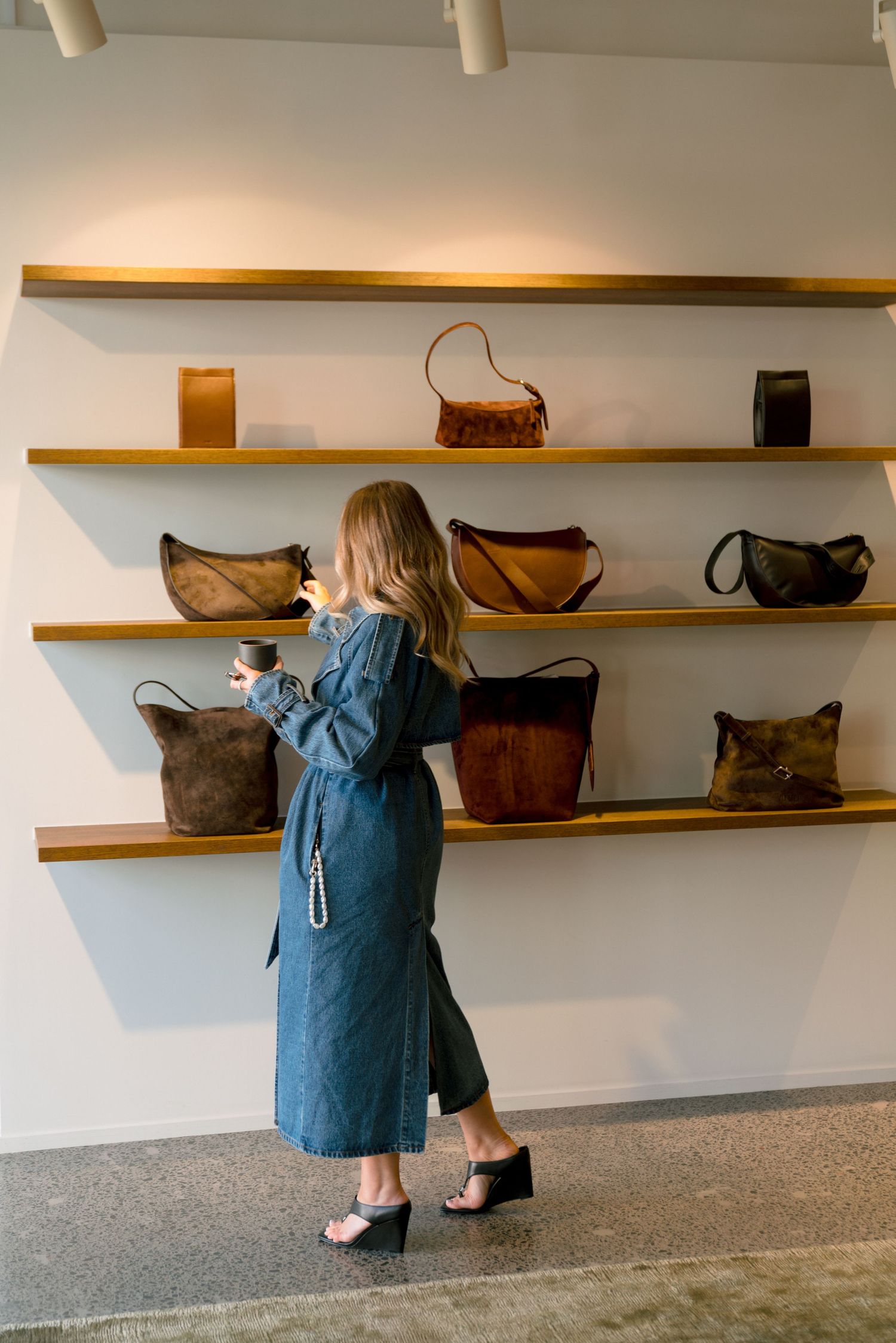 Artisanal leather handbags and purses displayed on minimalist wooden wall shelves in a gallery-like retail setting.