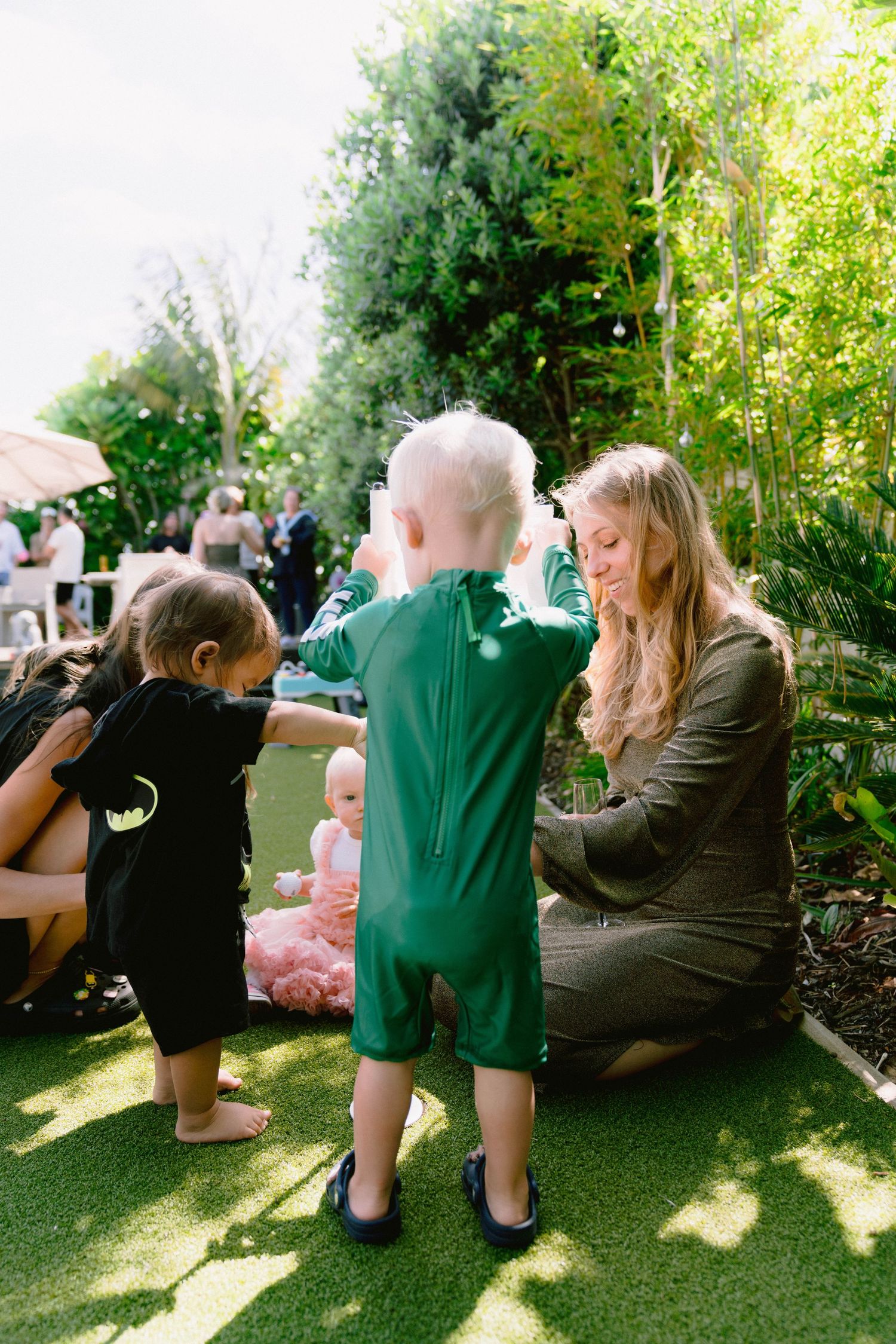 Young photographers with cameras capture moments in a sunlit garden setting during an outdoor event.