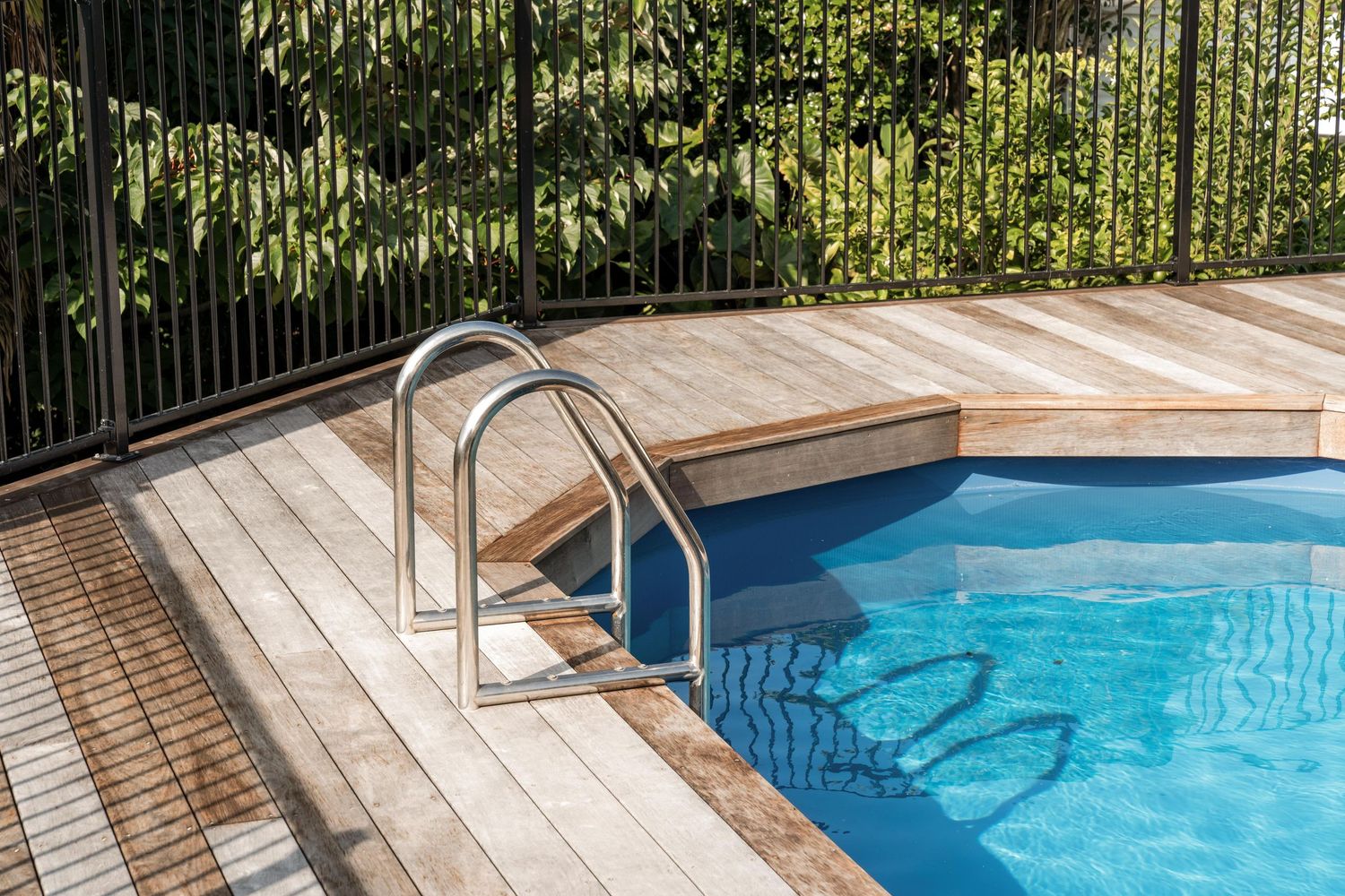 Close-up of swimming pool with wooden deck and metal ladder showing clear blue water.