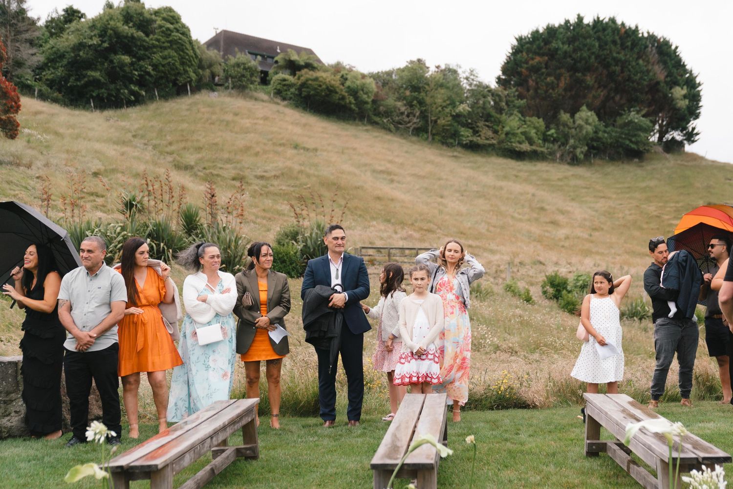 Wedding guests playing lawn games at an outdoor countryside reception on a sunny hillside.