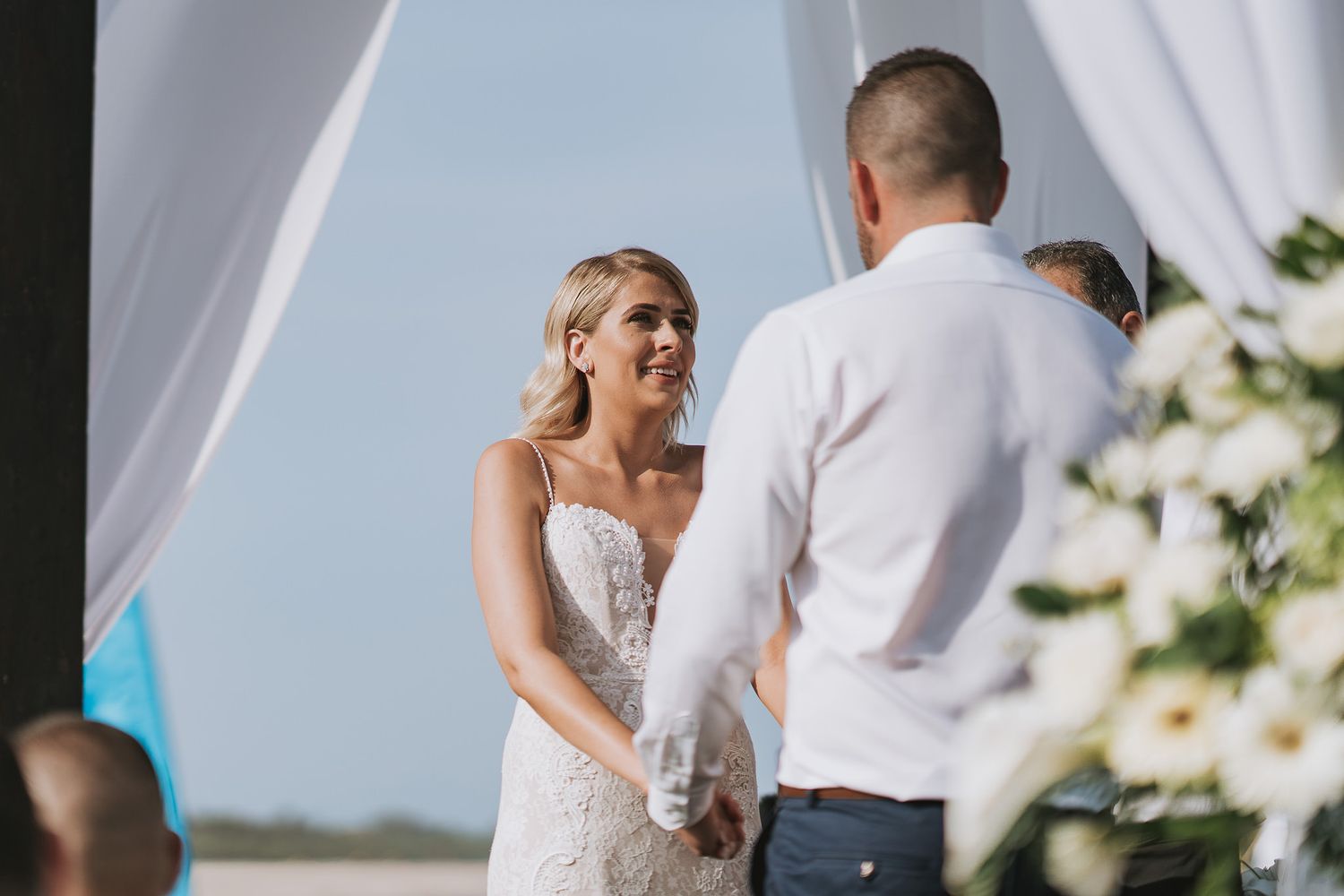 An intimate moment between a couple during their outdoor beach wedding ceremony with white draping and floral decor.