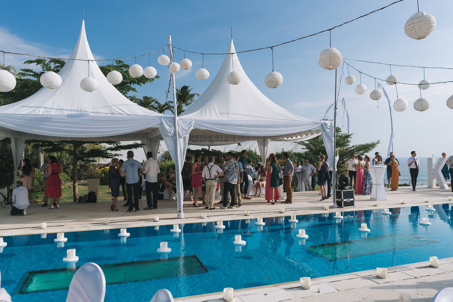 White tent pavilions and paper lanterns set up beside a swimming pool for an outdoor event.