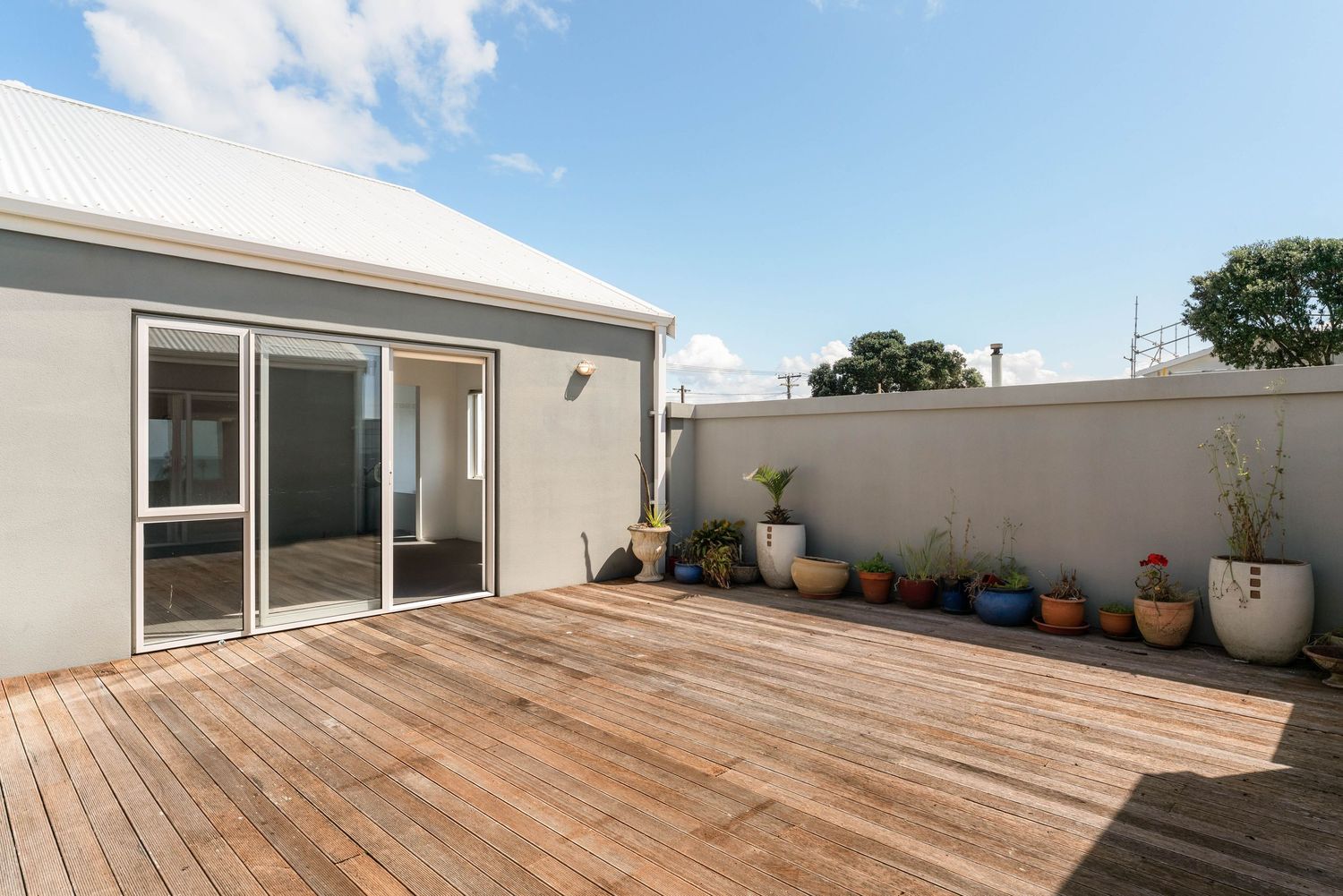 Spacious wooden deck terrace with potted plants and white exterior walls under blue sky.