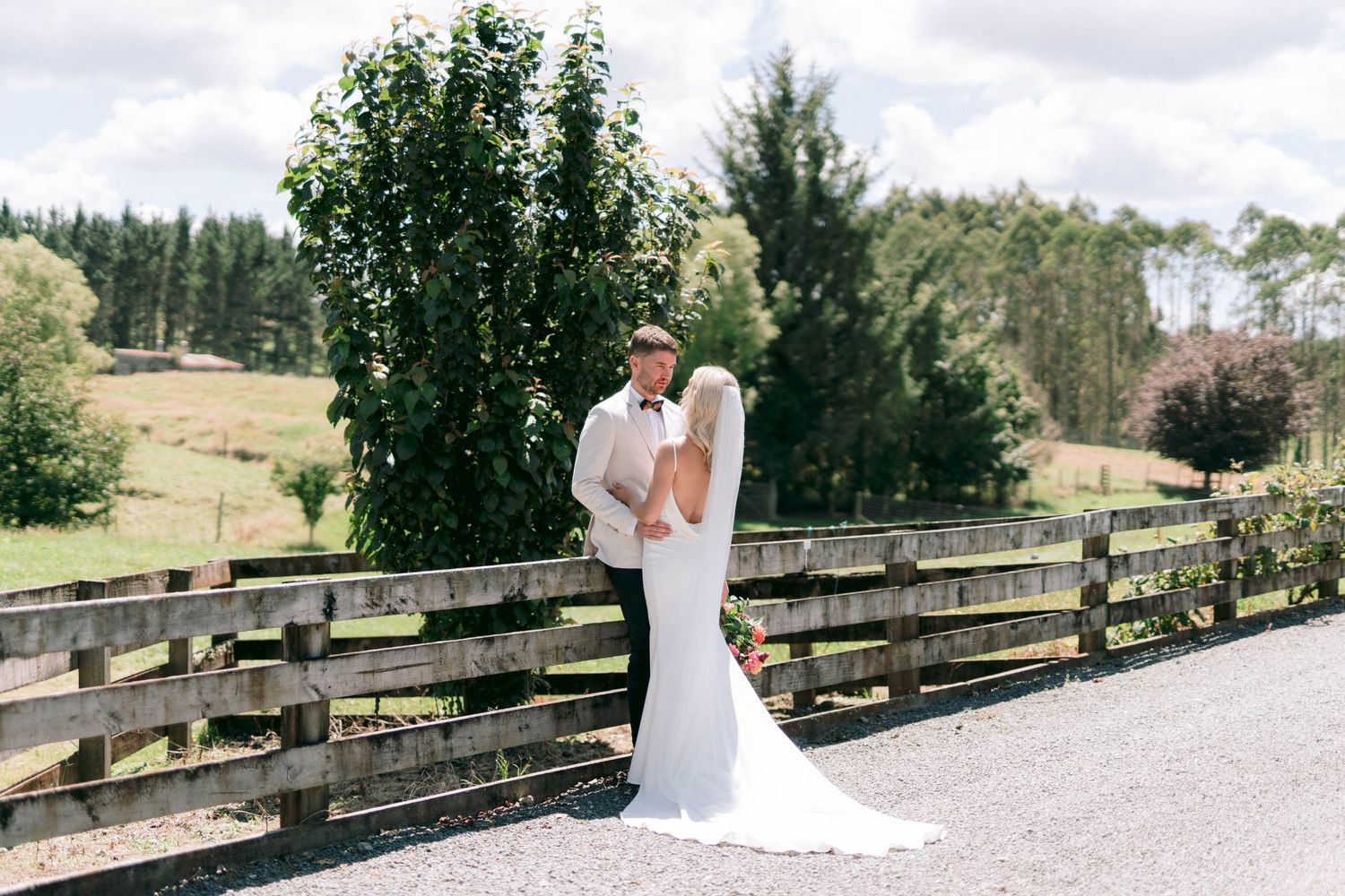 Couple sharing an intimate moment on a rustic wooden bridge overlooking green countryside on a sunny afternoon.