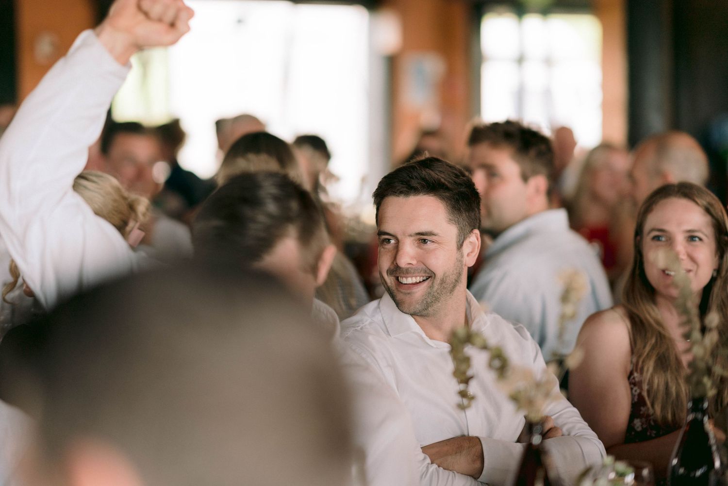Wedding reception guests celebrate with raised arms in indoor venue.