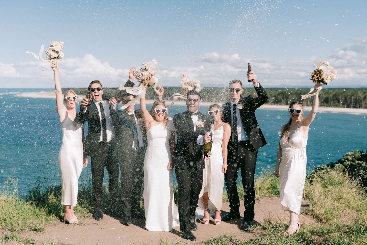 Joyful wedding celebration on a scenic bluff with ocean views and blue skies in the background.