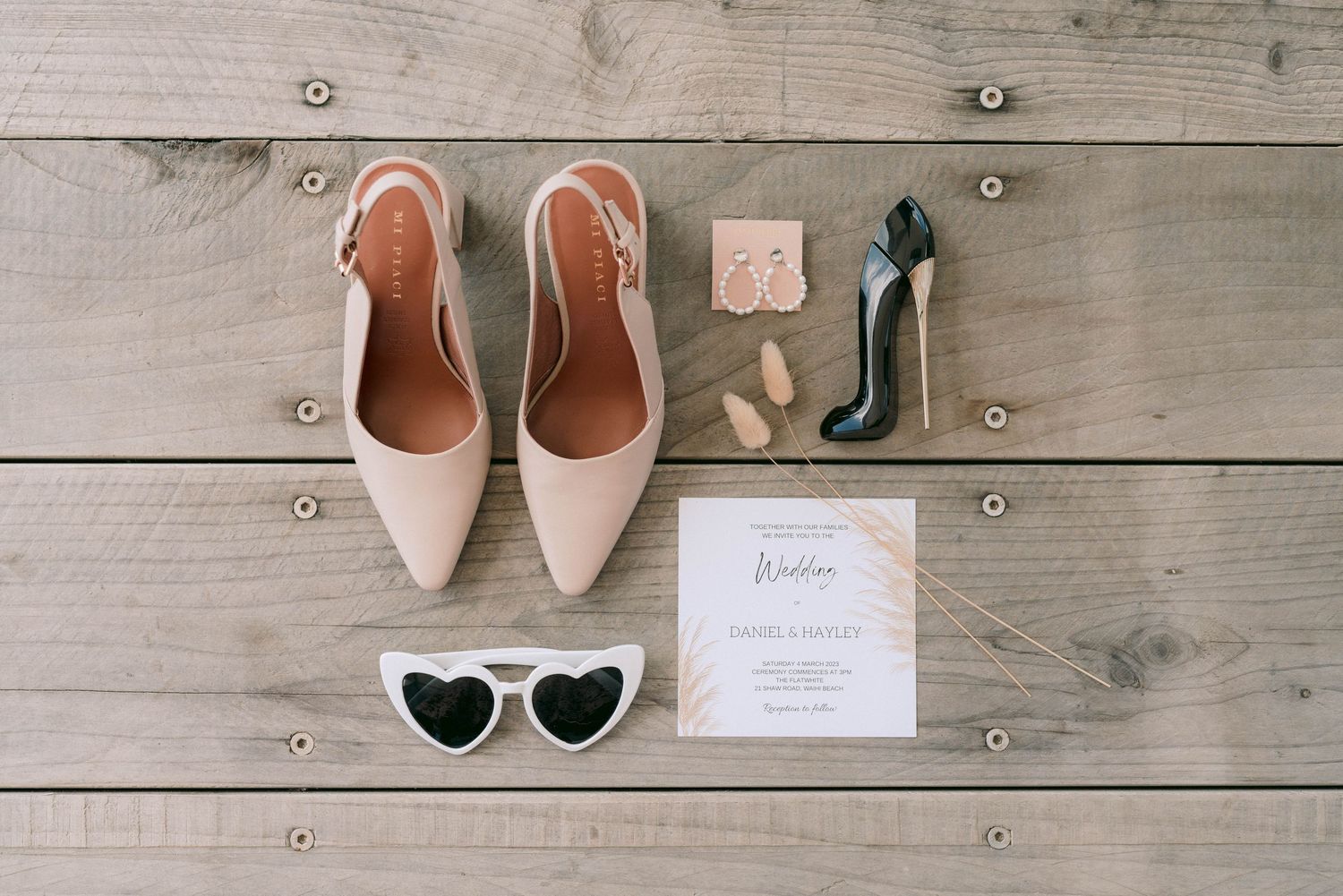 A stylish collection of women's footwear and sunglasses arranged on wooden floorboards in neutral tones.