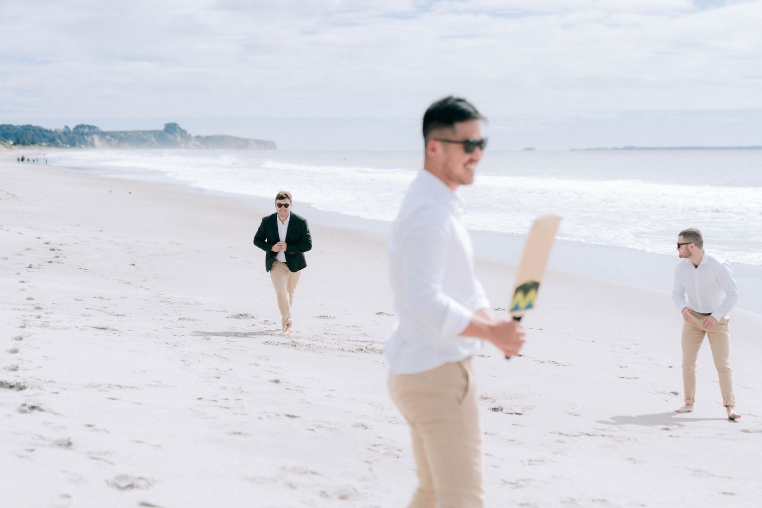 People walking and relaxing together on a sunny beach with white sand and cloudy sky in the background.
